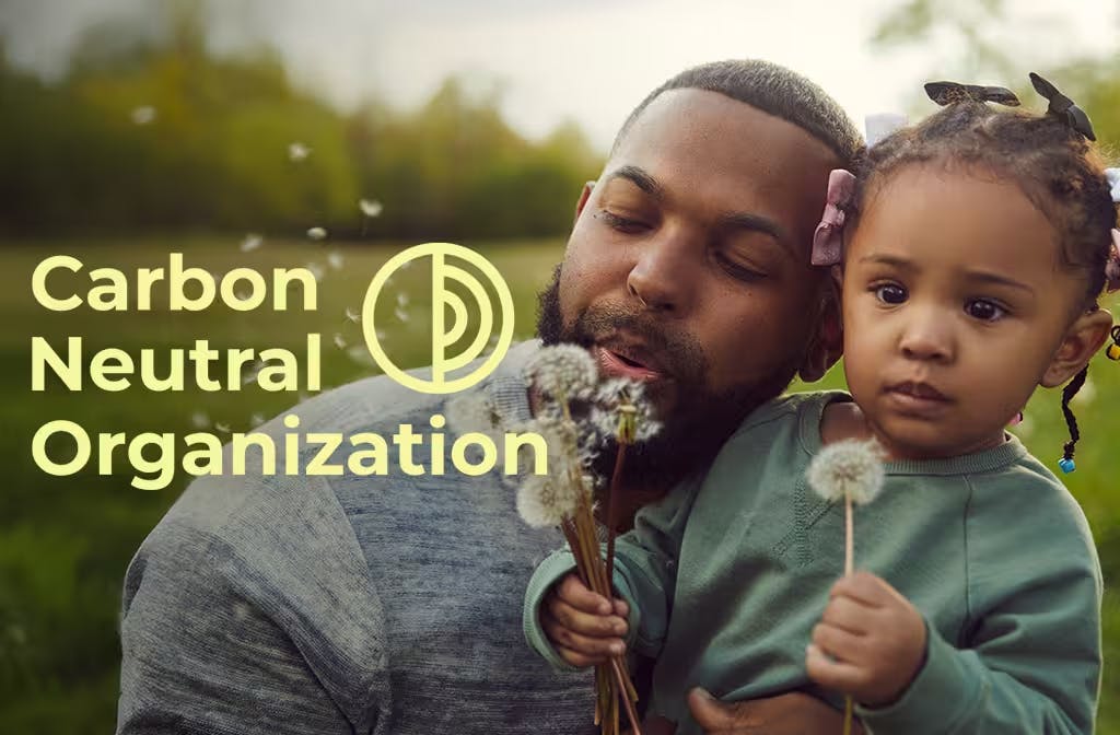 Father and young daughter blowing dandelions outdoors with Carbon Neutral Organization logo overlay