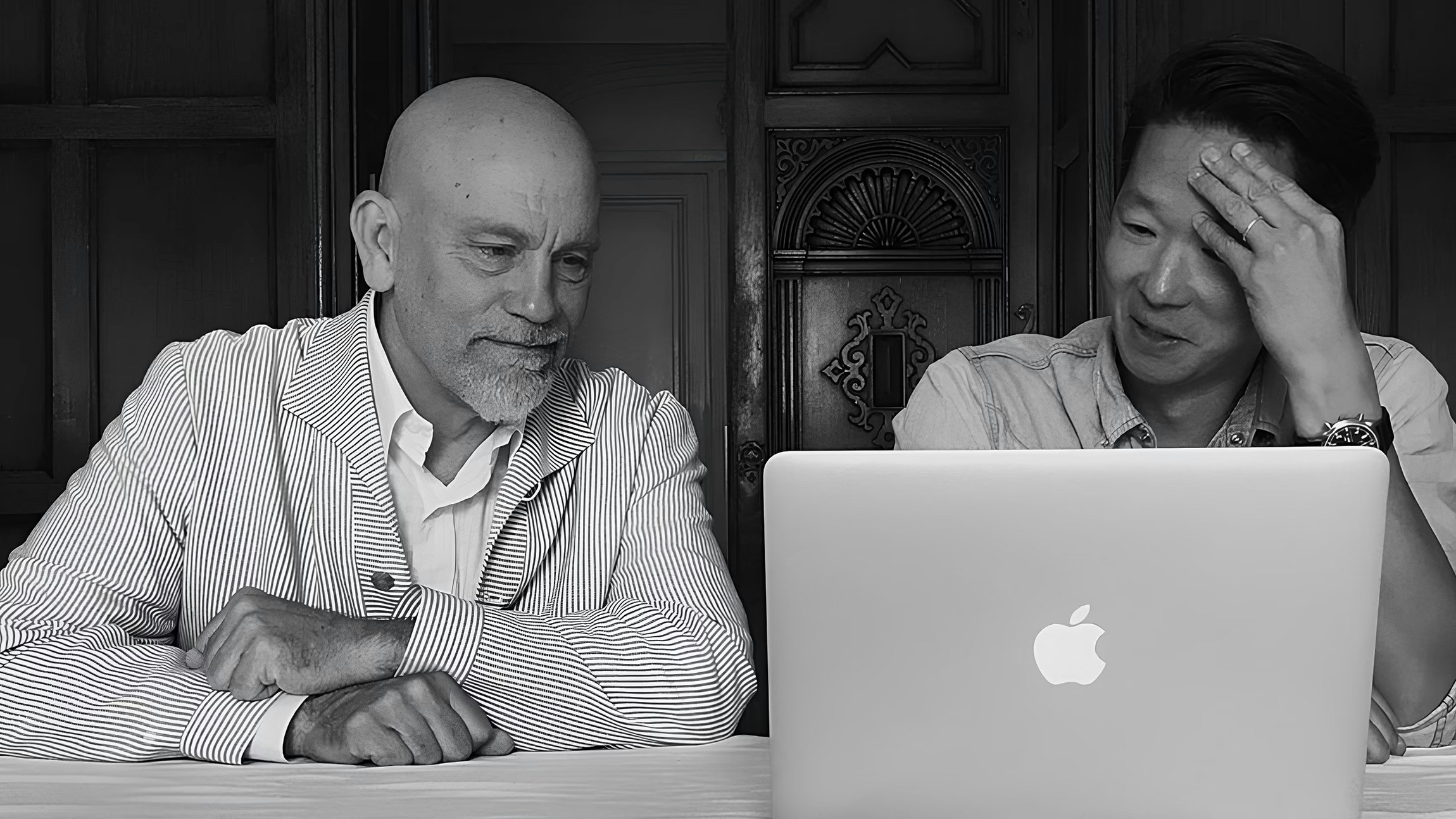 Two men at a laptop collaborating in black and white photo.