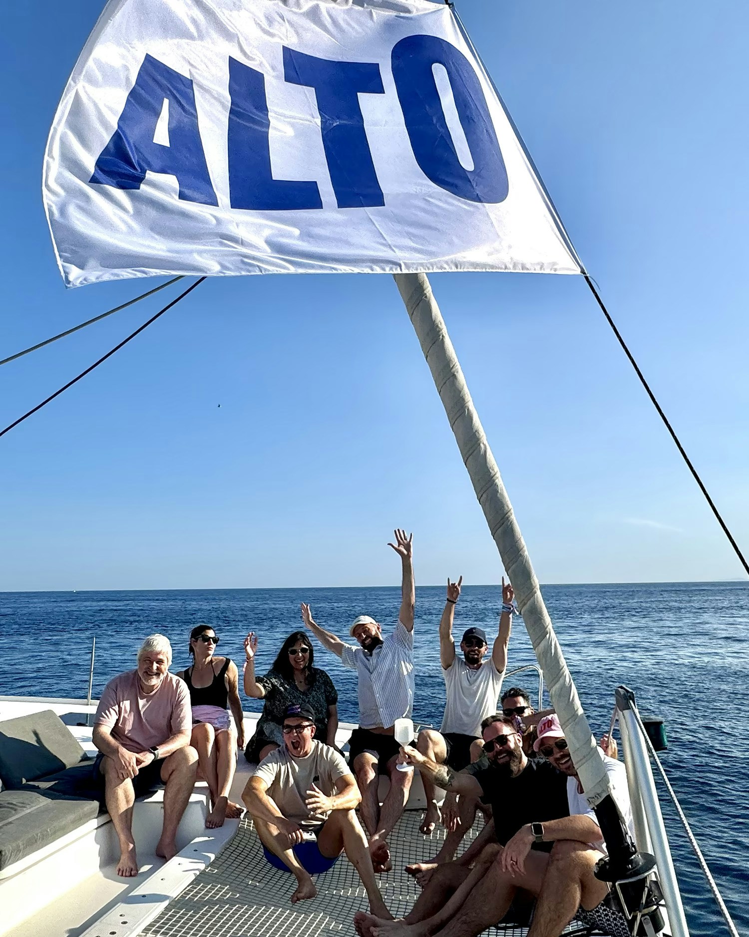Group celebrating on a sailboat with a large ALTO flag on a sunny day at sea
