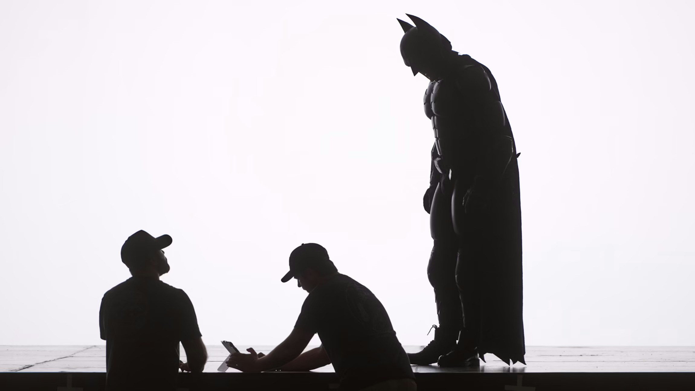 Behind-the-scenes silhouette of actor in Batman costume with crew on set