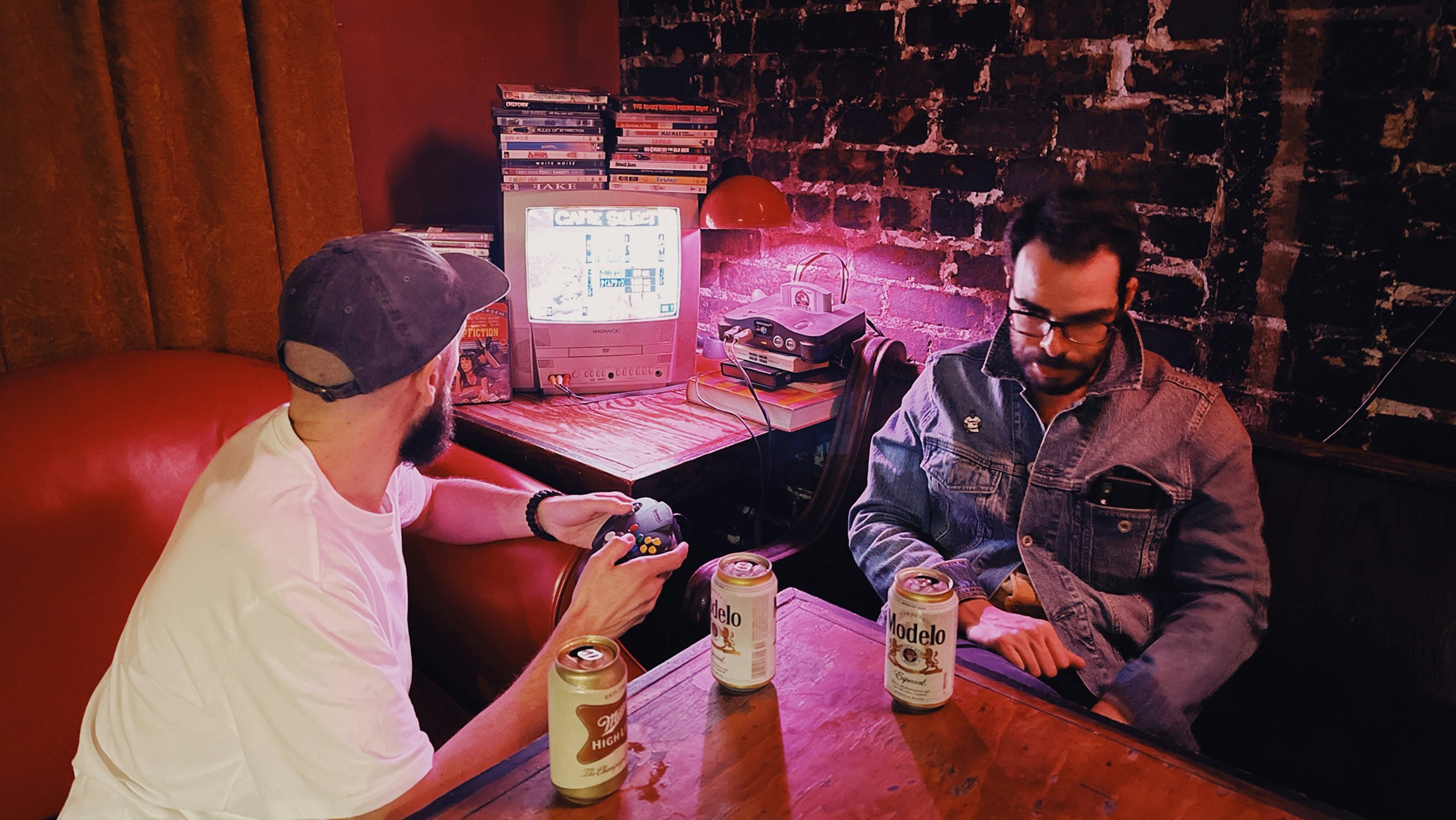 Two men playing retro video games in a dimly lit bar