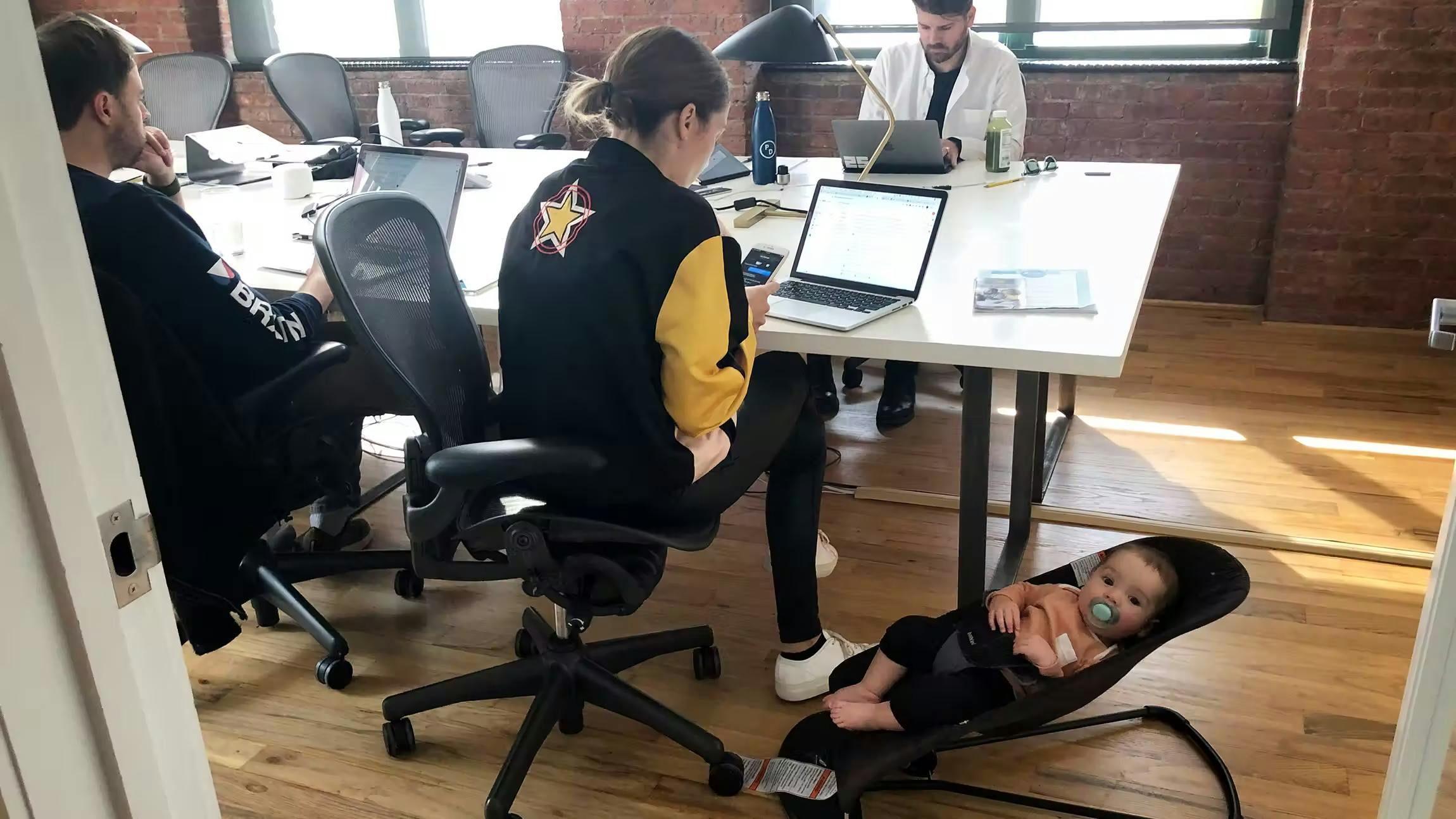 Casual day at Alto office with team members working at a table while a baby relaxes in a bouncer nearby