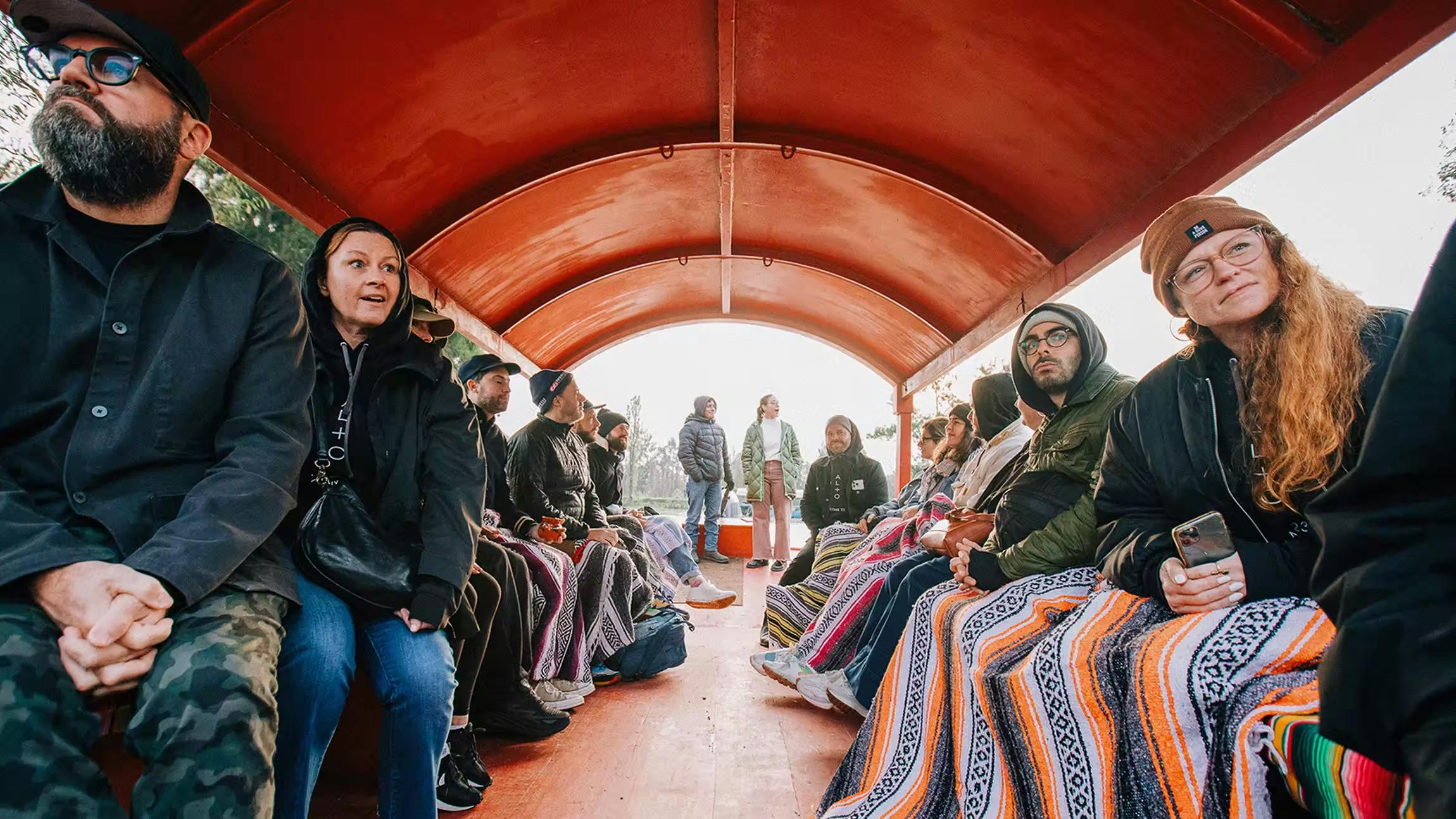 Alto team members bundled in colorful blankets during an outdoor group outing on a covered boat ride in Mexico City