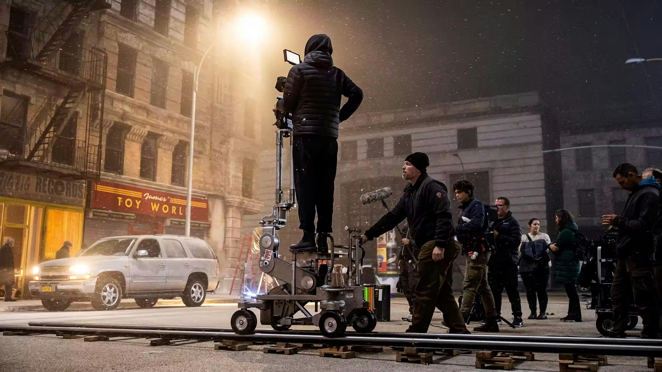 Behind the scenes of the Montefiore Einstein holiday television commercial shoot, with crew operating a camera on a dolly track during a snowy night city scene