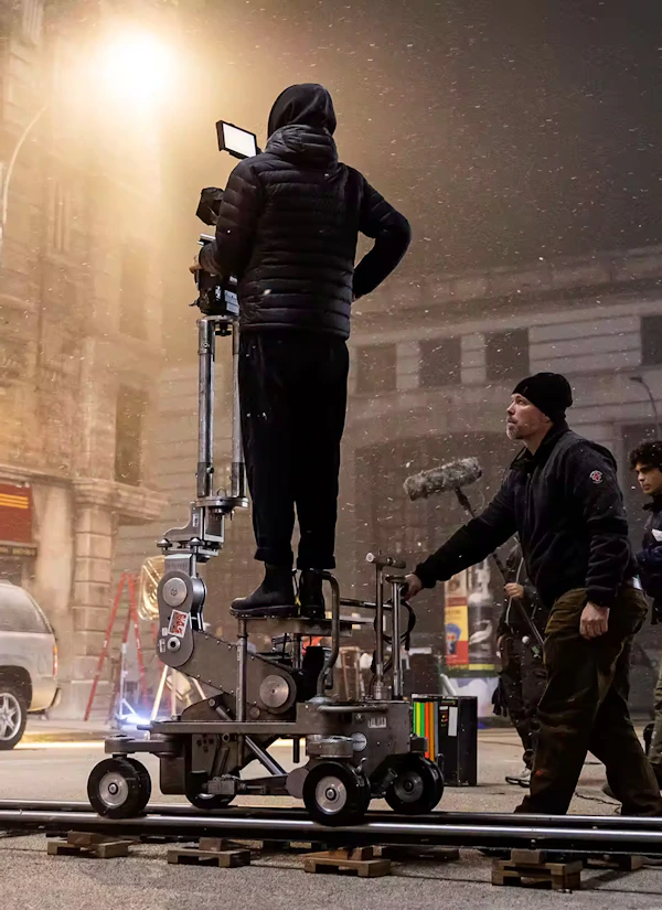 Behind the scenes of the Montefiore Einstein holiday television commercial shoot, with crew operating a camera on a dolly track during a snowy night city scene
