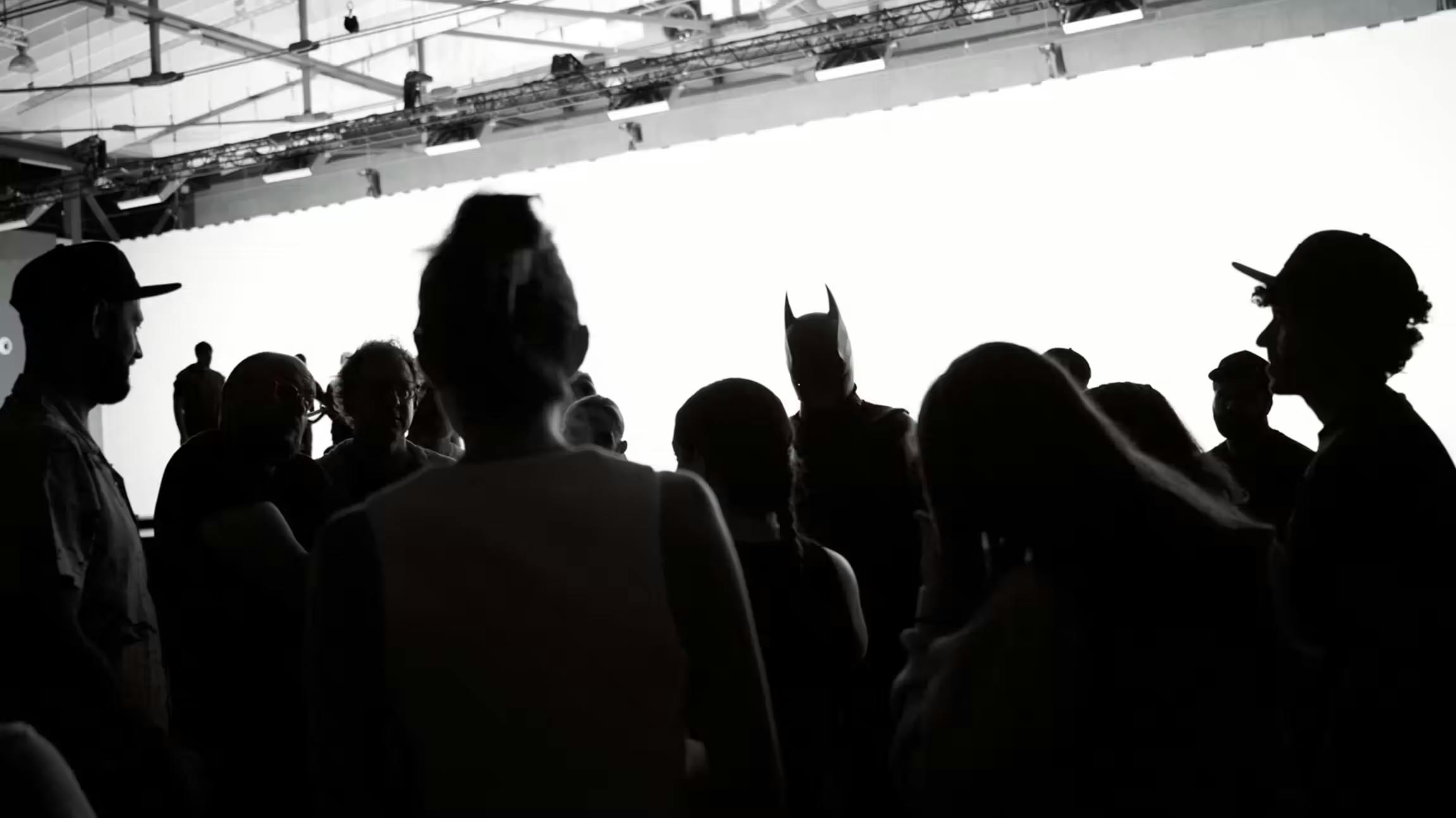 Silhouetted film crew gathered around an actor dressed as Batman on a brightly lit set during a behind-the-scenes production