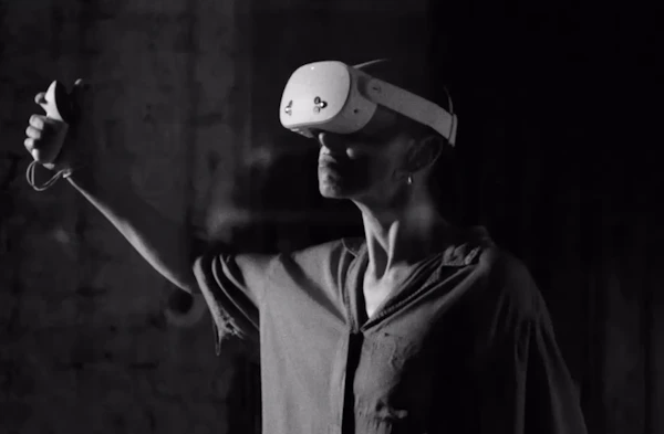 Person wearing a Meta Quest VR headset and holding a controller, immersed in a virtual reality experience in a dark room